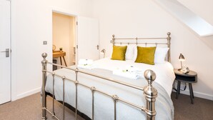 Een netjes opgemaakt slaapkamer met een metalen bed, een nachtkastje met een lamp en een deur naar een andere kamer.