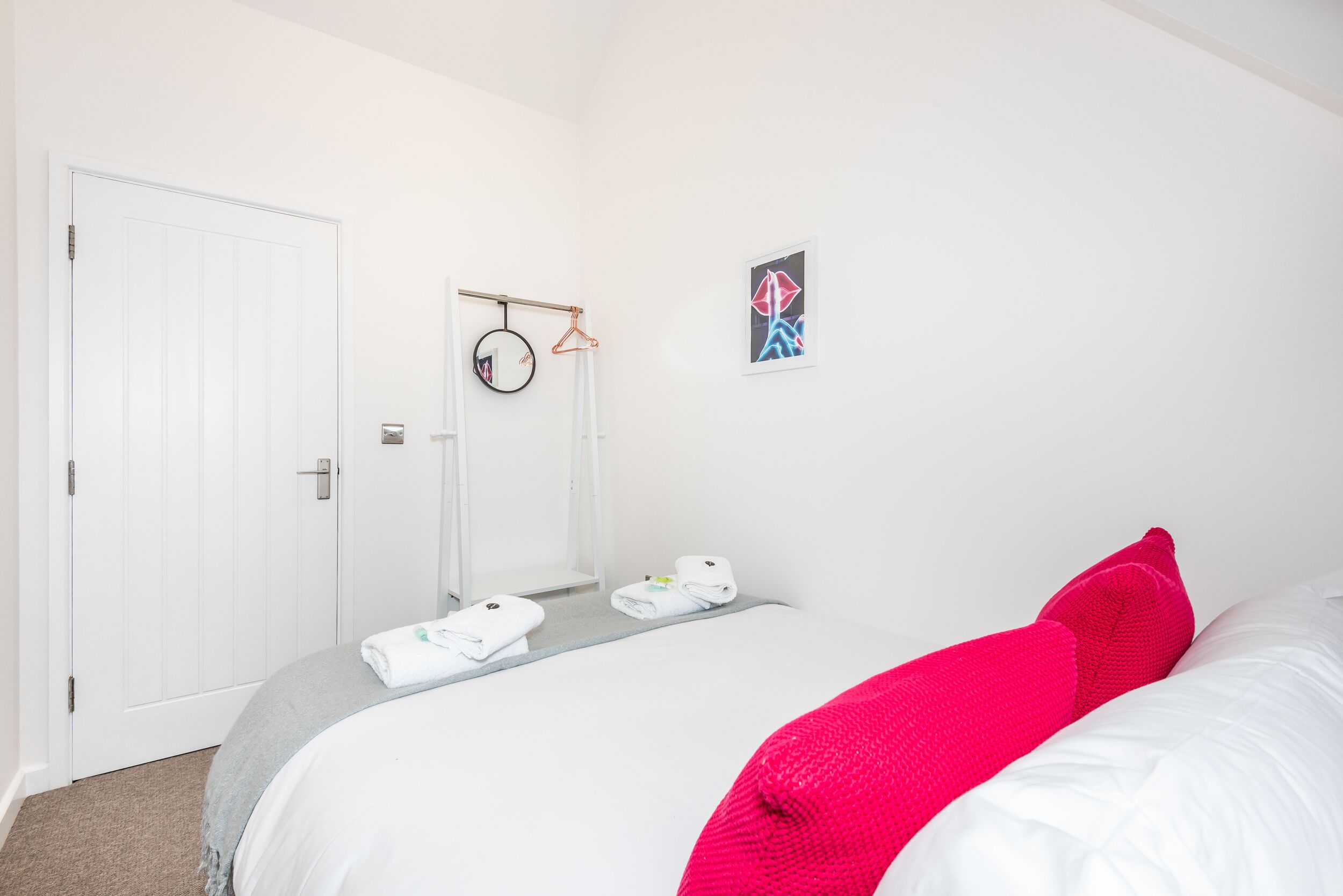 A hotel room with a bed, a door, a towel rack, and a framed picture on the wall.