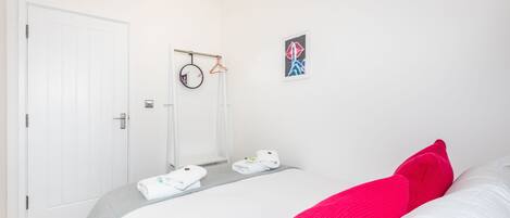 A hotel room with a bed, a door, a towel rack, and a framed picture on the wall.