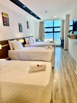 A hotel room with two beds, a large window with a view, and a flat-screen TV mounted on the wall.