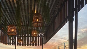 An outdoor seating area with a view of the sunset over the water, featuring wicker chairs, a sofa, and hanging lights. - Sun Hotel (Encarnacion)