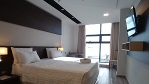 A modern hotel room with a large bed, a flat-screen TV mounted on the wall, and a large window offering a view of the city. - Sun Hotel (Encarnacion)