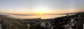 A panoramic view of a coastal cityscape during sunset with a prominent bridge and a stadium in the foreground.