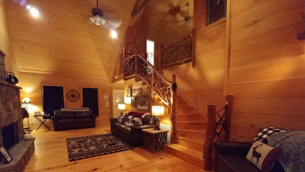 Interior acogedor de una cabaña de troncos con chimenea, sofás de cuero, una escalera y paredes de madera.