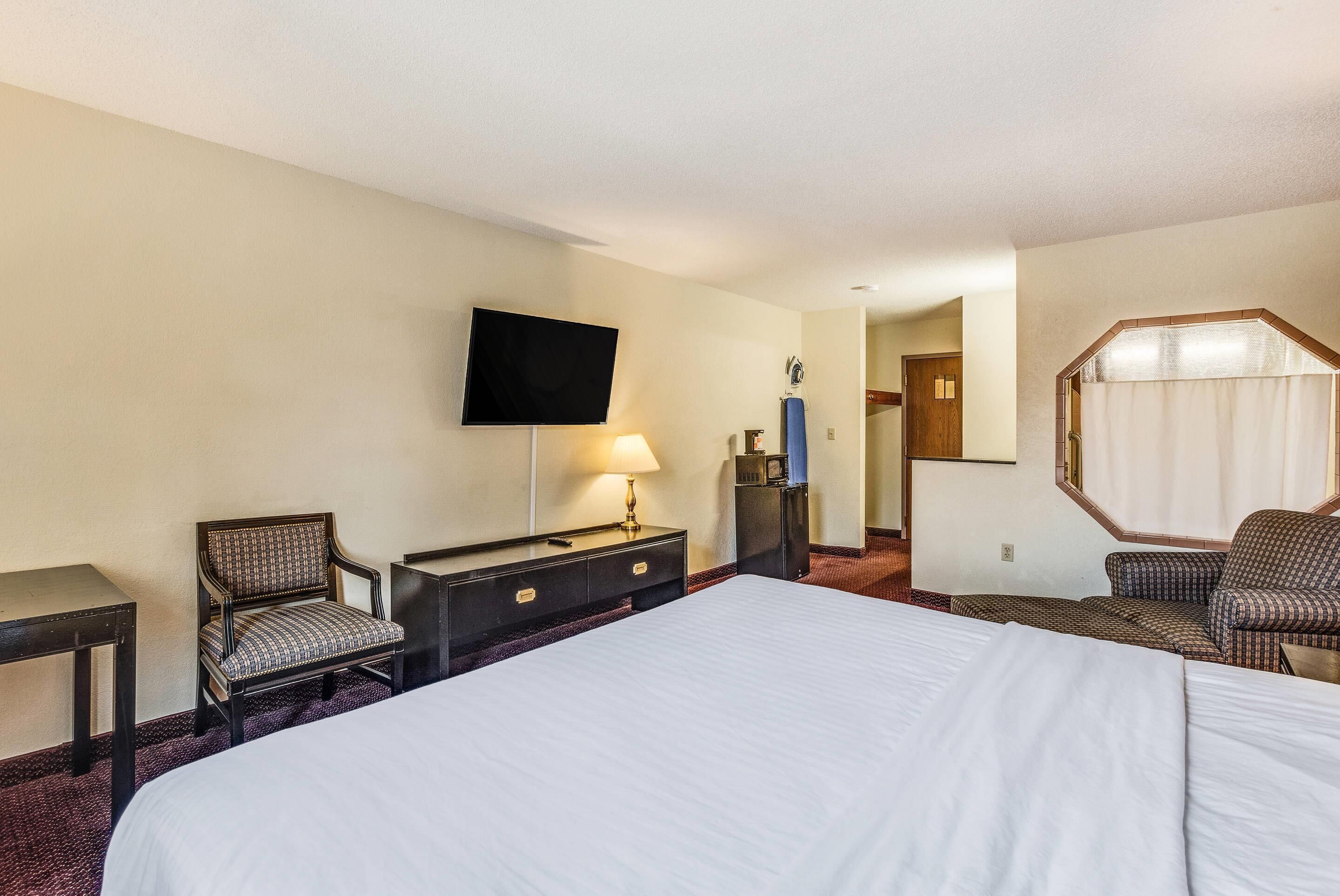 A hotel room with a large bed, a desk with a lamp, a television, and a seating area with a chair and a sofa.