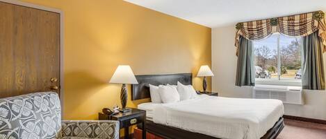 A hotel room with a bed, bedside tables, a chair, and a window with curtains.