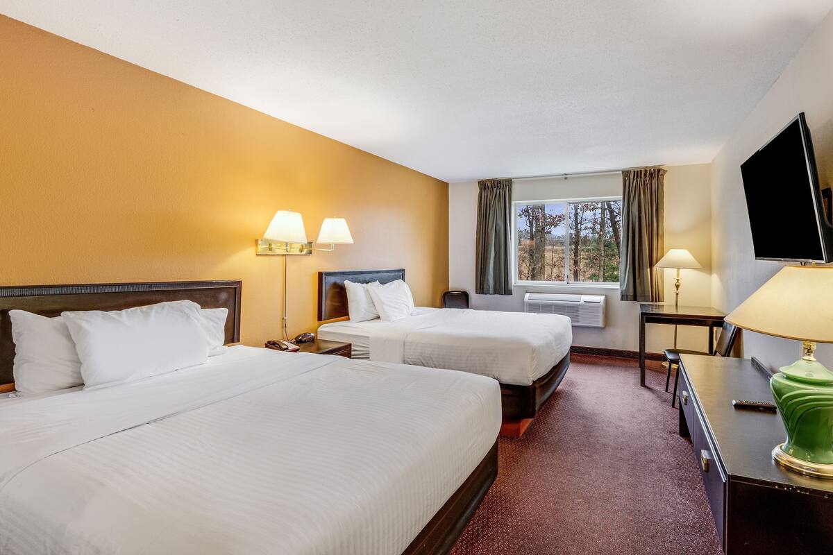 A hotel room with two beds, a desk, a chair, a TV, and a window with curtains.