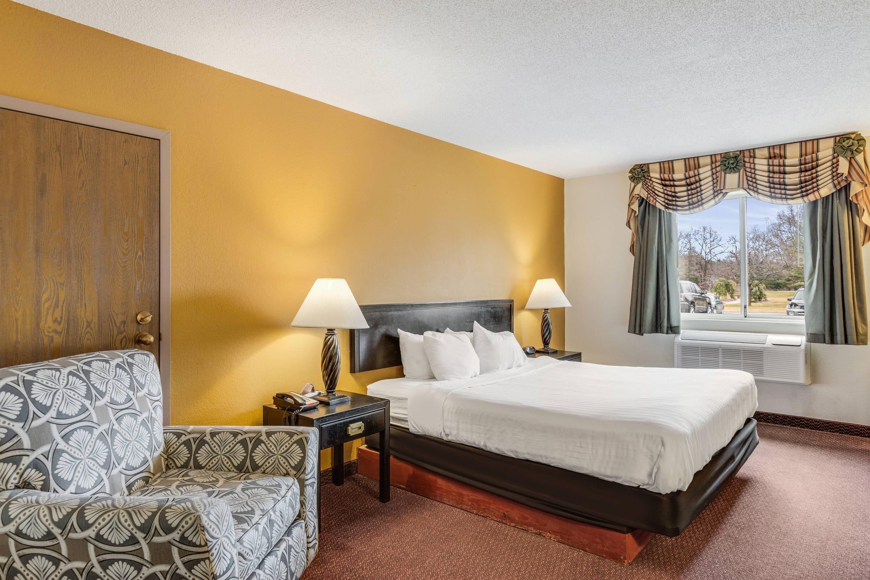 A hotel room with a bed, bedside tables, a chair, and a window with curtains.