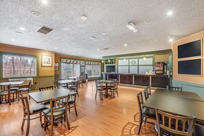 A restaurant with wooden tables and chairs, a bar area, and large windows with blinds. - Econo Lodge Whitehall near Michigan's Adventure (Whitehall)