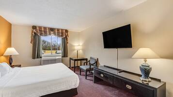 Habitación de hotel con cama, escritorio, silla, televisión y ventana con cortinas.