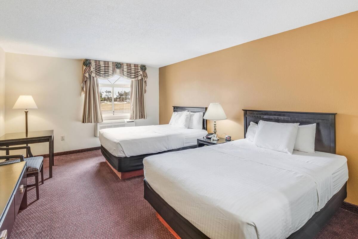 A hotel room with two beds, a desk, a chair, and a window with curtains.