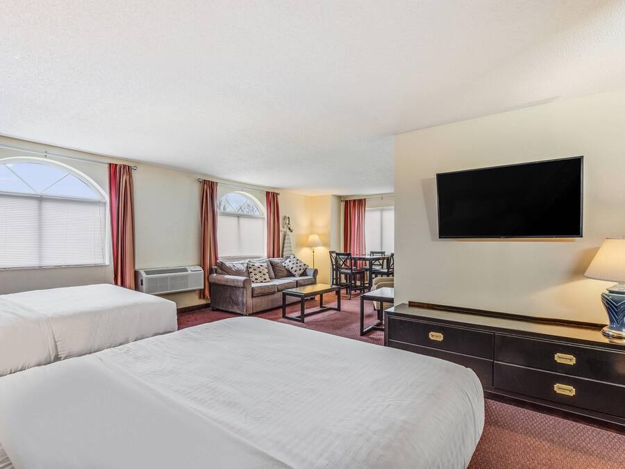 A hotel room with two beds, a sofa, a desk, and a TV.
