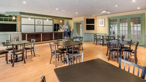 A dining area with multiple tables and chairs, a kitchen area with appliances, and a clock on the wall. - Econo Lodge Whitehall near Michigan's Adventure (Whitehall)