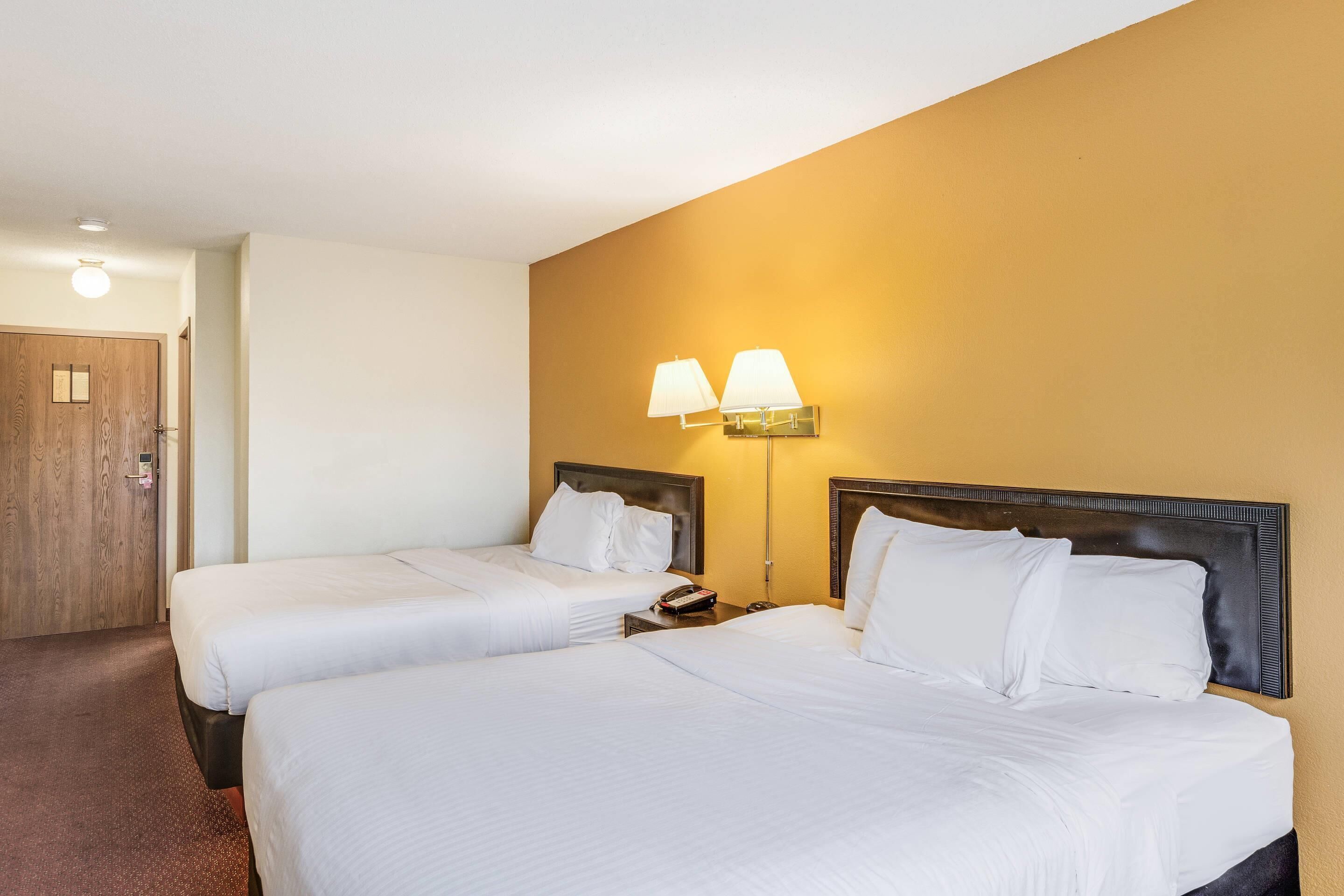 Une chambre d’hôtel avec deux lits, une porte en bois et une lampe fixée au mur.
