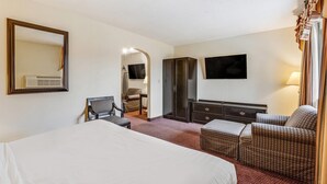A hotel room with a large bed, a seating area with a sofa and chairs, a television, a wardrobe, and a mirror. - Econo Lodge Whitehall near Michigan's Adventure (Whitehall)