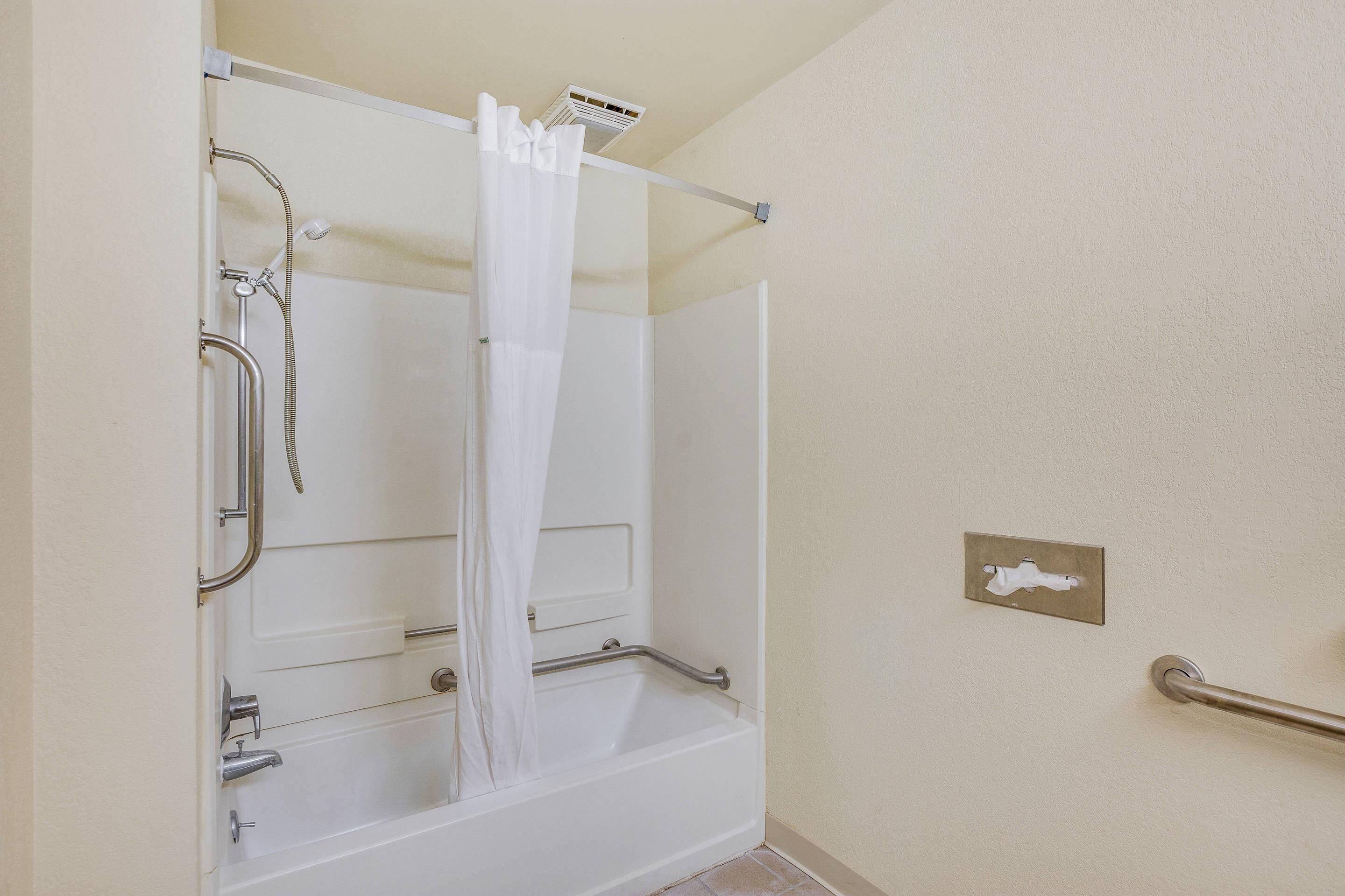 A bathroom with a bathtub, shower, and handrails.