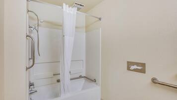 A bathroom with a bathtub, shower, and handrails.