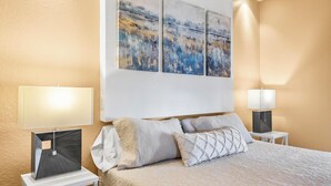 Quarto bem arrumado com uma cama, duas mesas de cabeceira e três quadros pendurados na parede.