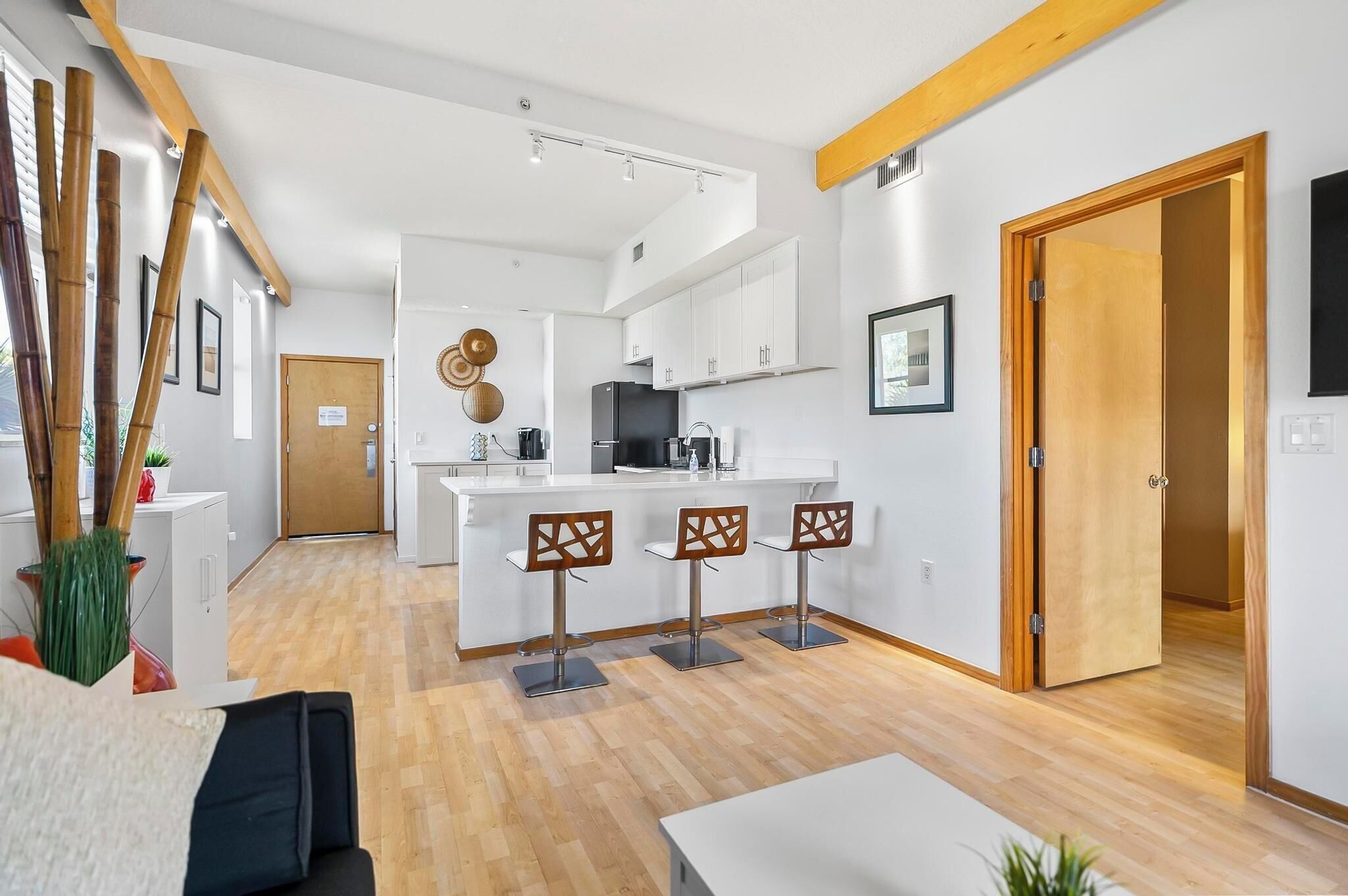 A modern kitchen with white cabinets, a central island with bar stools, and a wooden ceiling beam.