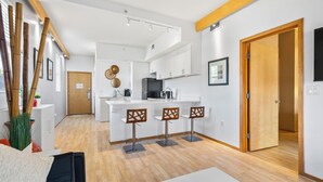 Cozinha moderna com armários brancos, uma ilha central com banquetas e um vigamento de madeira.