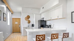 Cozinha moderna com armários brancos, uma ilha grande com banquetas e uma porta de madeira ao fundo.