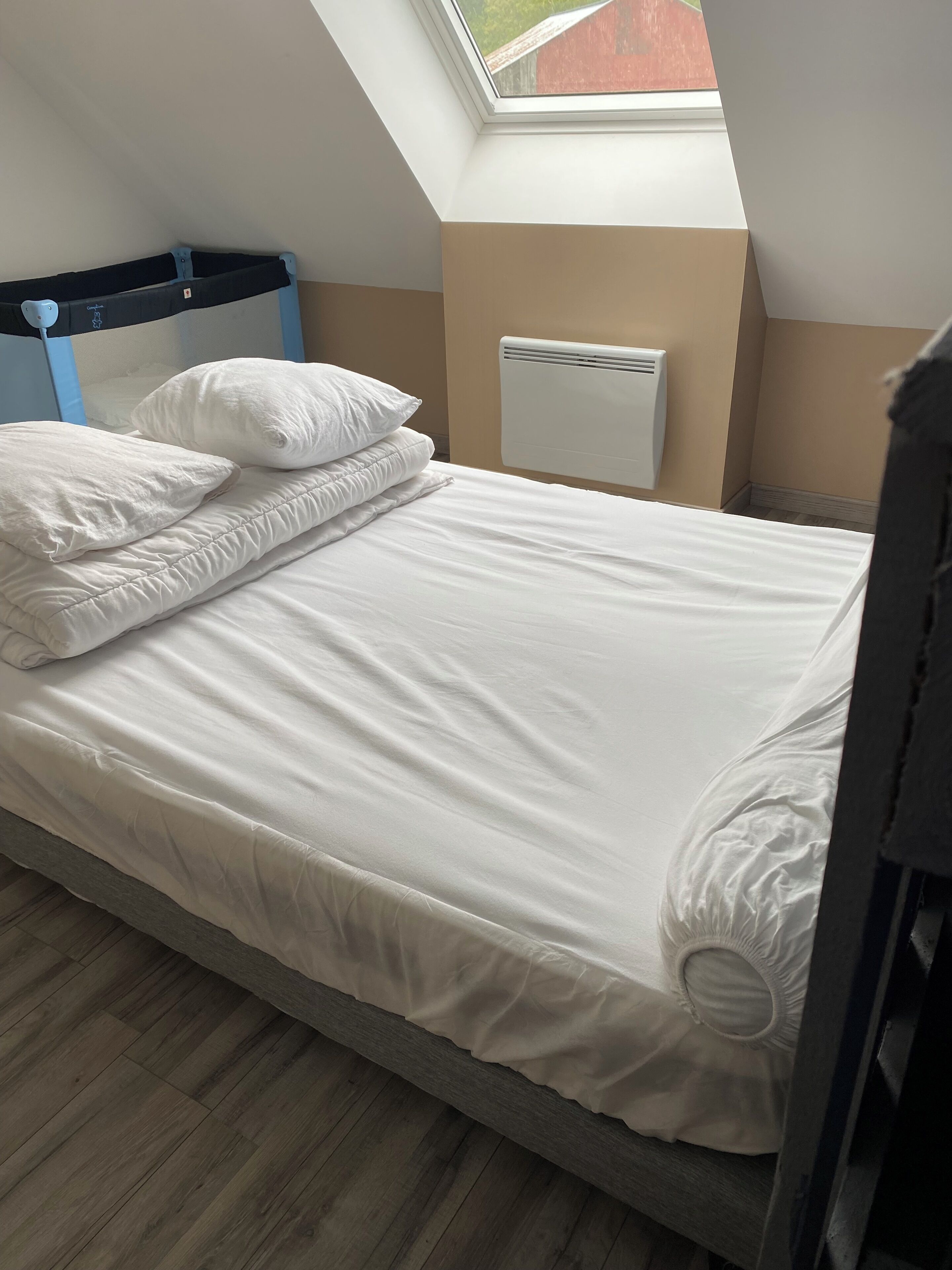 A neatly made bed with white bedding in a room with a sloped ceiling and a skylight.