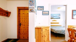 Una habitación con puerta de madera, un mueble pequeño, una cama con colcha azul estampada y una silla de madera.