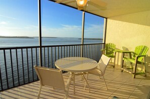 A balcony with a view of the sea, a round table, two chairs, and a ceiling fan.