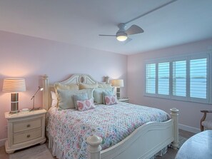 A bedroom with a bed, nightstands, a ceiling fan, and a window with blinds.