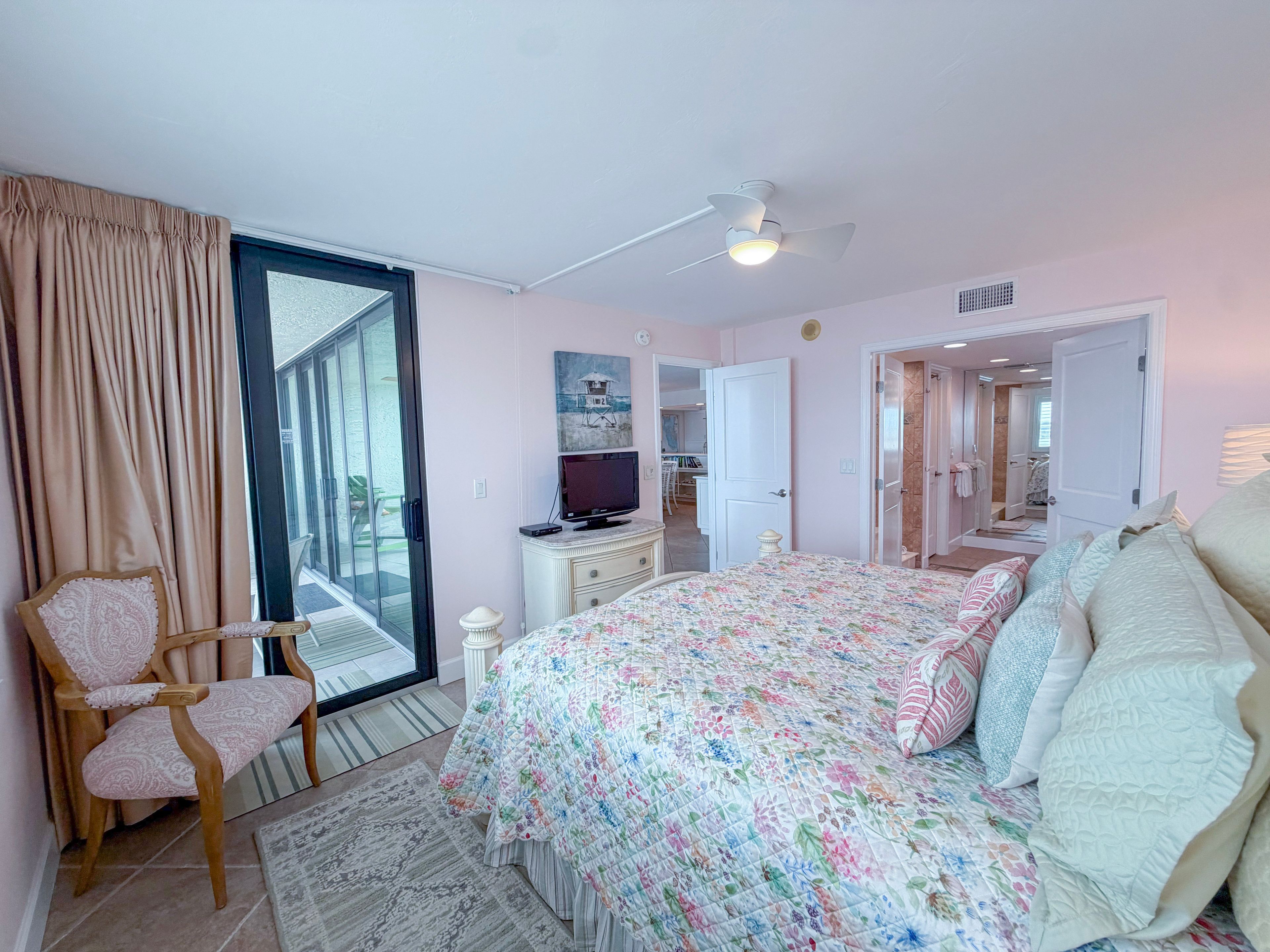 Une chambre à coucher comprenant un lit, une chaise, un téléviseur et une porte donnant sur une salle de bain.