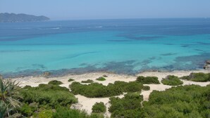 Paisaje costero con aguas turquesas cristalinas, playa arenosa y vegetación verde exuberante.
