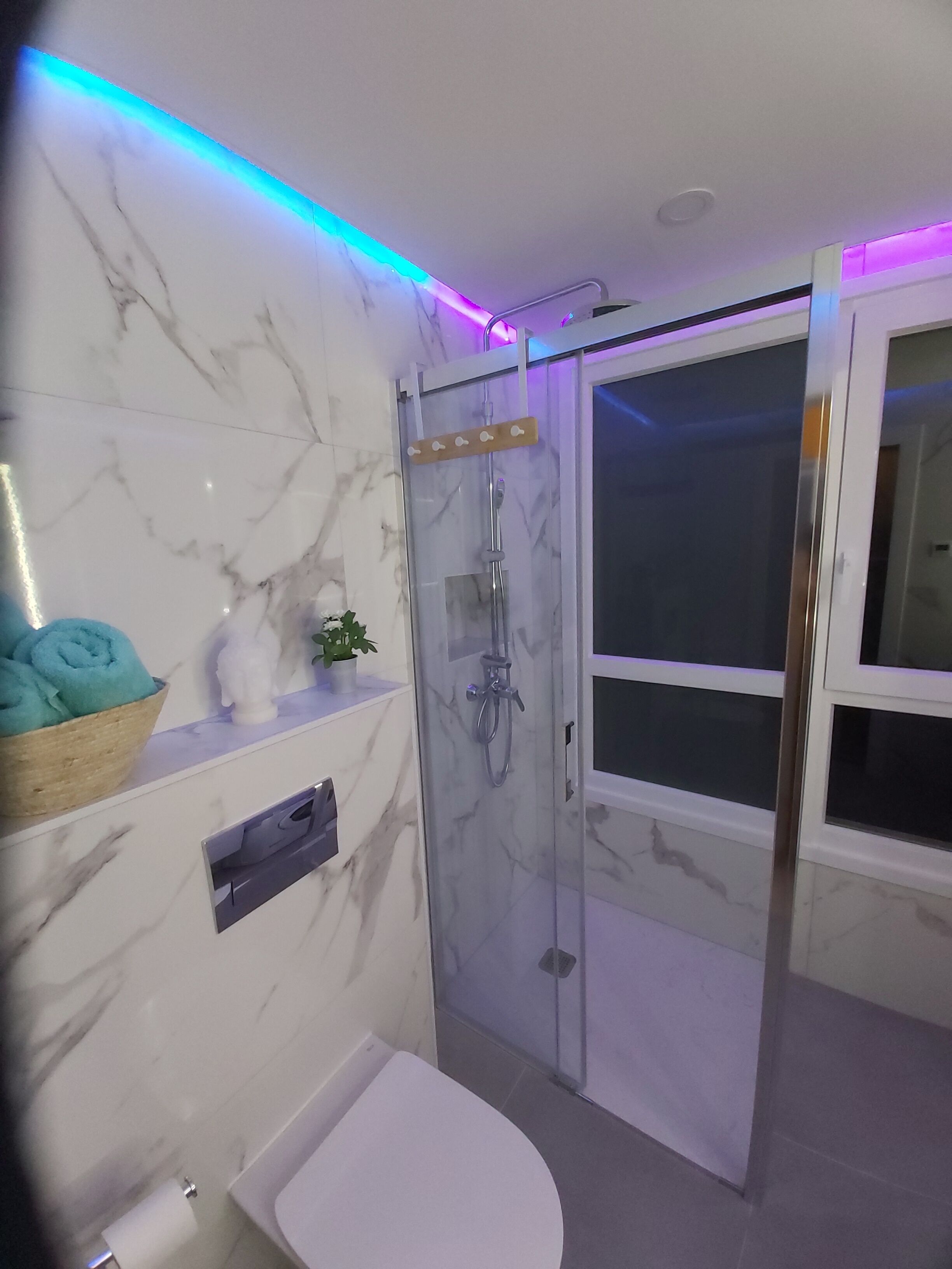 Ein modernes Badezimmer mit einer gläsernen Duschkabine, Marmorwänden und einer weißen Toilette.