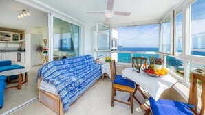 Un balcón con vistas al mar, una zona de comedor con mesa y sillas, y un sofá.