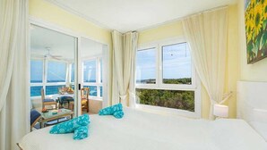 Habitación de hotel con una cama grande, vistas al mar y un balcón con mobiliario exterior.