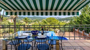 Un área de comedor al aire libre con una mesa lista para cuatro personas, rodeada de sillas, bajo un toldo a rayas.