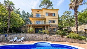 Una casa de dos pisos con piscina, muros de piedra y un balcón.