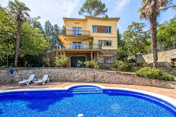 A two-story house with a swimming pool, stone walls, and a balcony.