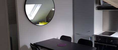 A compact kitchen with a dining area, including a foldable table and chairs, a round mirror, and a built-in oven.