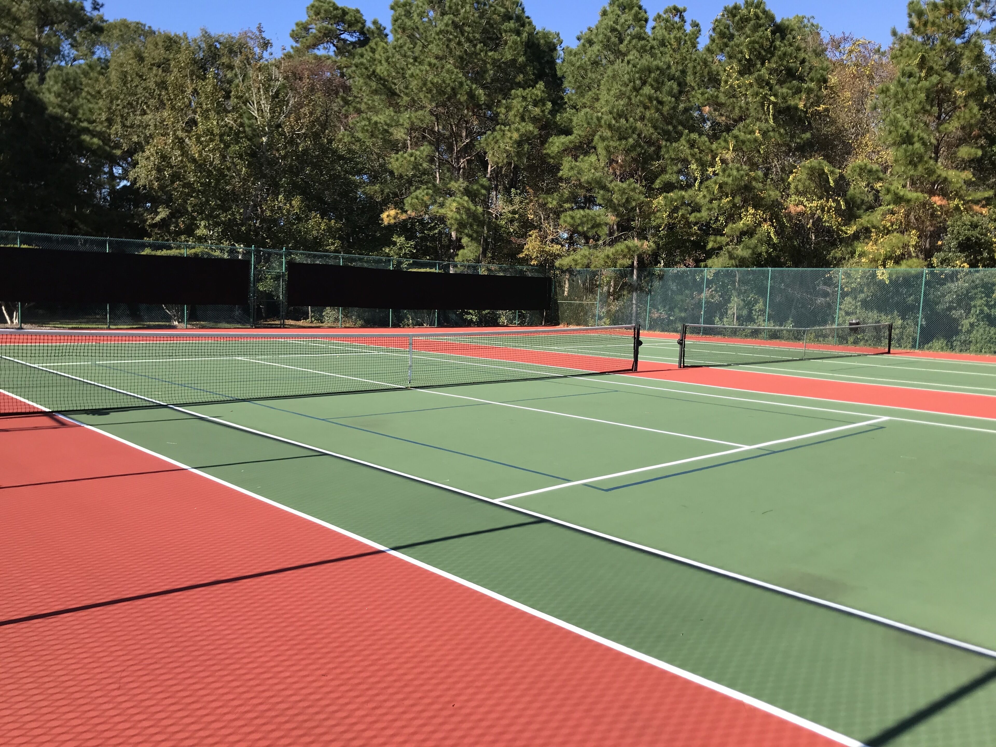 A tennis court with a net, surrounded by trees and a fence.