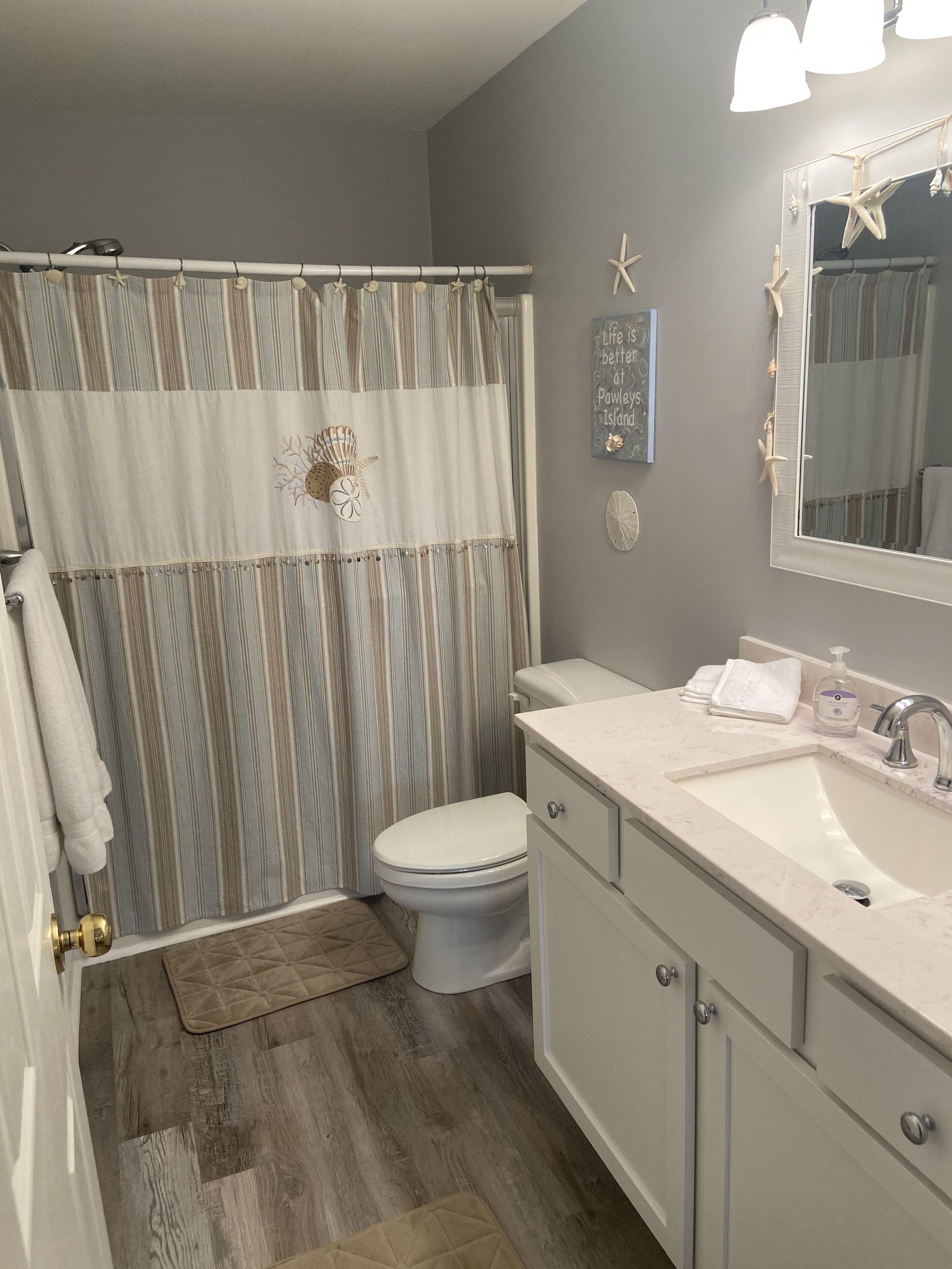 A bathroom with a shower curtain, toilet, sink, and vanity.