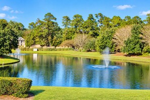 A tranquil pond with fountains, surrounded by well-maintained grass and trees, and a building in the background.