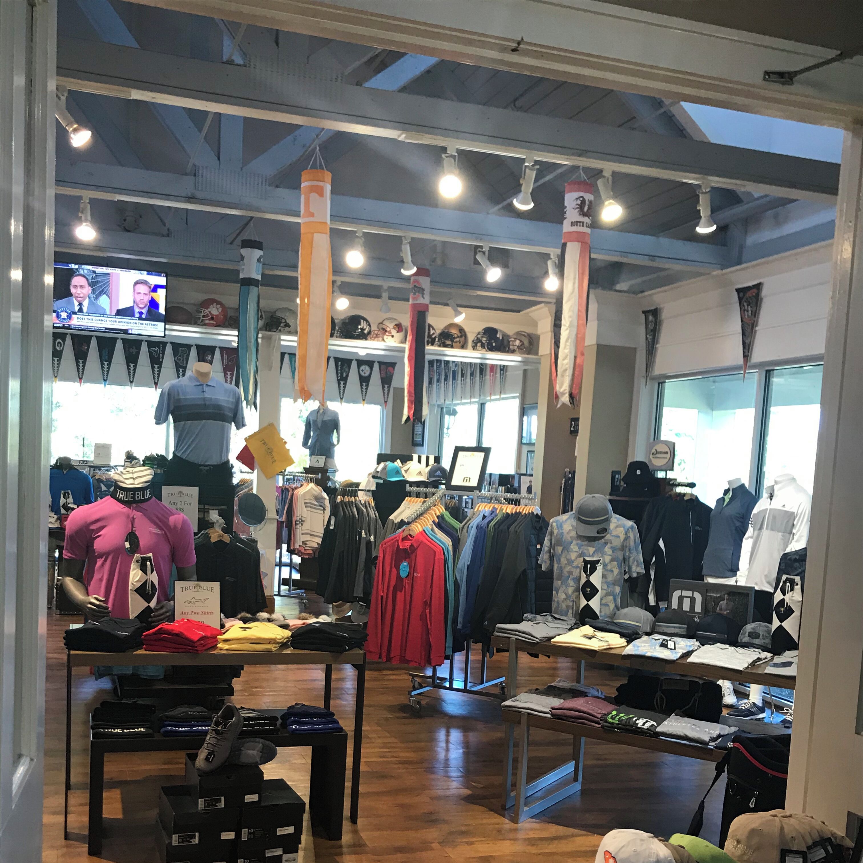 A clothing store with racks of shirts and pants, mannequins displaying outfits, and a TV screen in the background.