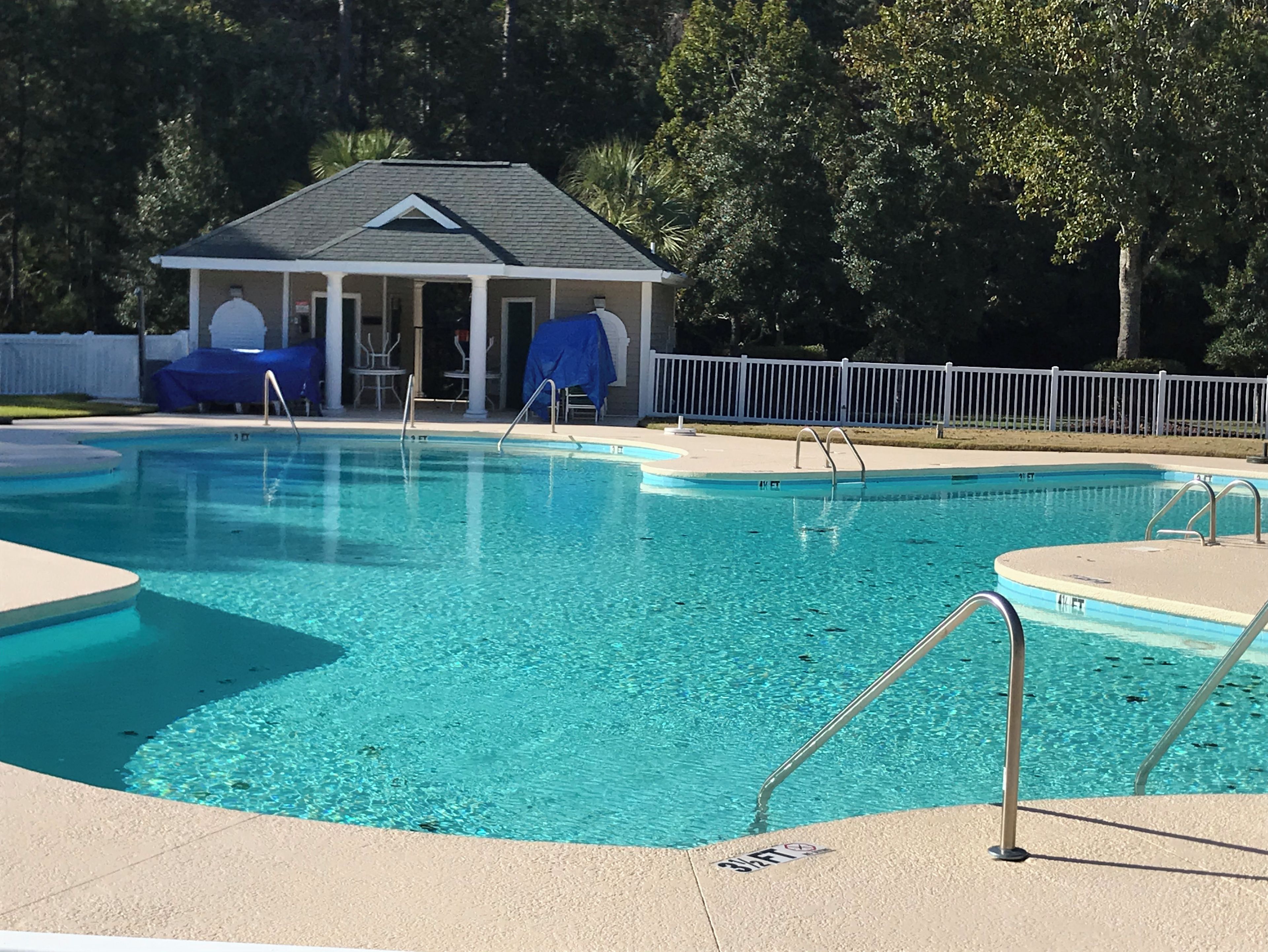 A clear swimming pool with a covered pavilion and lounge chairs in the background.