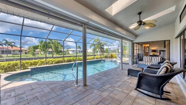 A spacious indoor pool area with a clear view of the surrounding neighborhood, a ceiling fan, and a seating area with a sofa and chairs. - Punta Gorda Isles 3 Bedroom Private Pool+Spa Home on Canal (Punta Gorde)