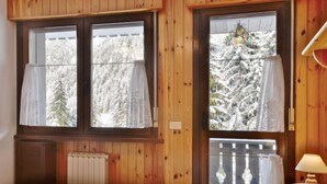 A bedroom with a bed, two windows with curtains, a radiator, and a lamp. - Des Alpes by Interhome (Canazei)