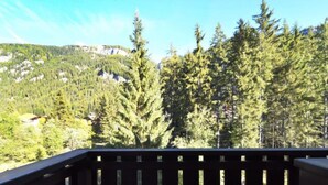 A balcony with a view of a forested mountain and a building in the distance. - Des Alpes by Interhome (Canazei)