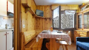 A wooden cabin interior with a dining table set for four, a blue sofa, and a television mounted on the wall. - Des Alpes by Interhome (Canazei)
