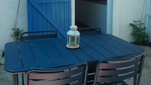 Un conjunto de mesa y sillas azules bajo un paraguas celeste, con una puerta blanca que da a una cocina.