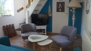 Una sala de estar con televisor, dos sillones grises, una mesa de centro blanca y una escalera.