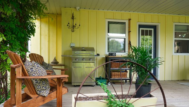 Een veranda met schommelstoelen, een barbecue en een bloembak op wielen.